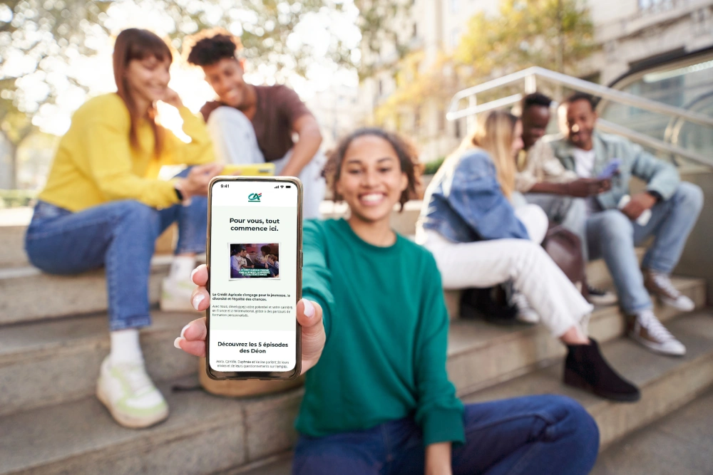 Groupe d'adolescent sur un banc, l'un est sur son téléphone et montre le site Rejoindre le Crédit Agricole